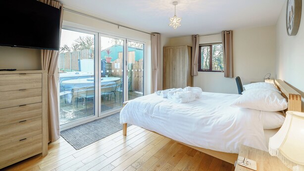 A bedroom with a bed, a TV, a wooden dresser, and a sliding glass door leading to an outdoor area. - 4 bedroom accommodation in Inglewhite, near Longridge (Inglewhite, near Longridge)