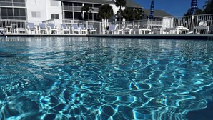 Ein klares Schwimmbecken mit Wellen, ein weißes Gebäude mit Balkonen und Palmen im Hintergrund.