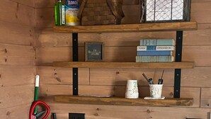 Una cuina compacta amb microones i nevereta, prestatges de fusta amb llibres i productes de neteja, i una escombra recolzada contra la paret.
