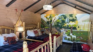 Habitació acollidora d'estil cabana amb dos llits de fusta, un mural de bosc i un sostre de fusta rústic.