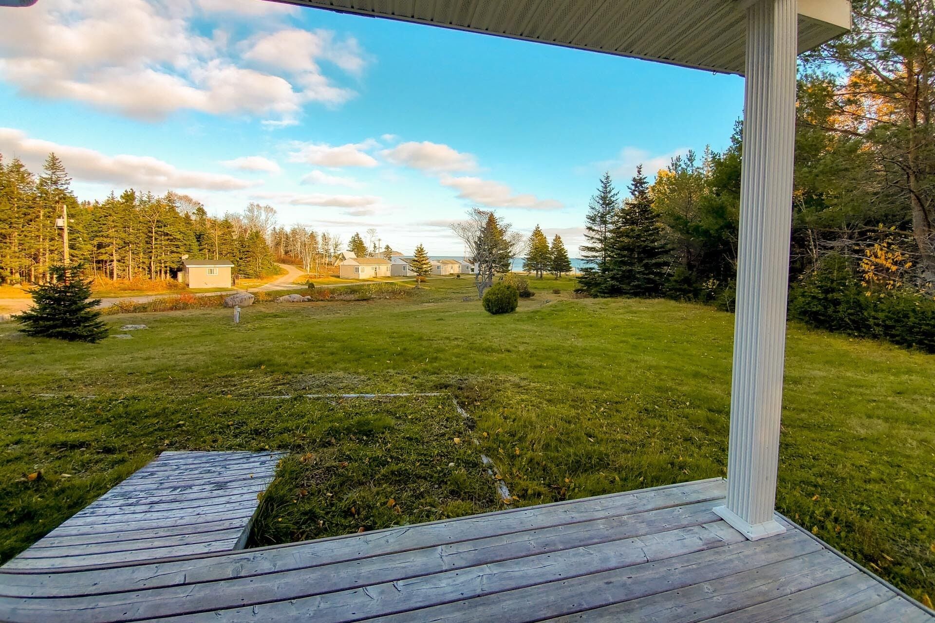 A wooden deck with a view of a grassy area, trees, and houses in the distance.