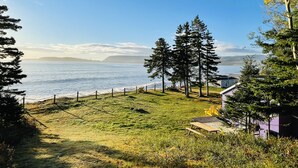 A grassy area with a view of the sea and mountains in the distance. - Glenghorm Beach Resort (Ingonish)