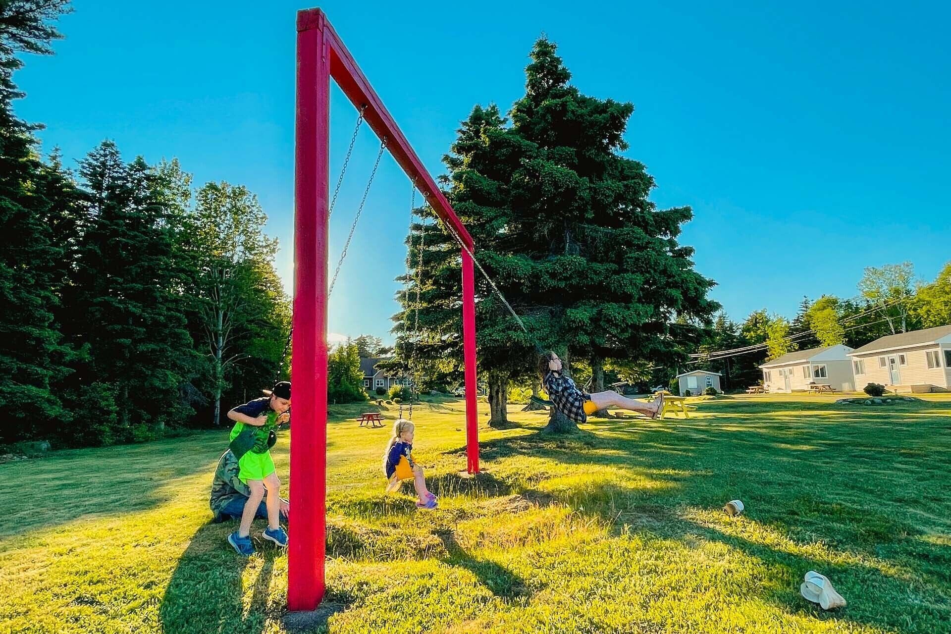 A playground with red equipment, a grassy area, and houses in the background.