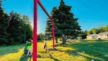 A playground with red equipment, a grassy area, and houses in the background.