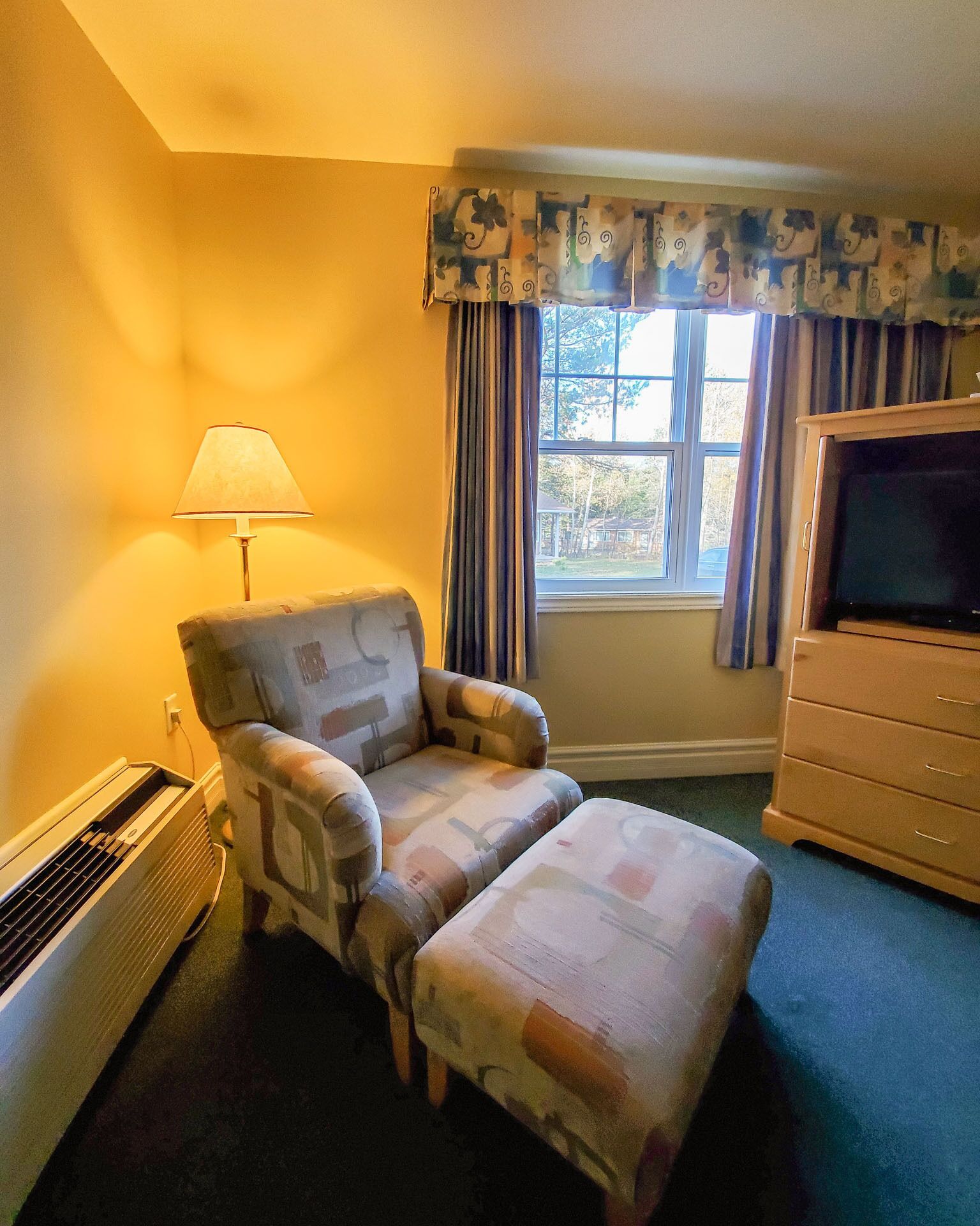 Una habitación con sofá, televisión, calefactor y ventana con cortinas.