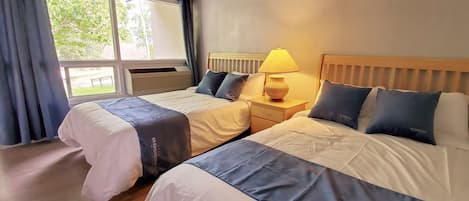 A hotel room with two beds, a nightstand with a lamp, and a window with curtains.
