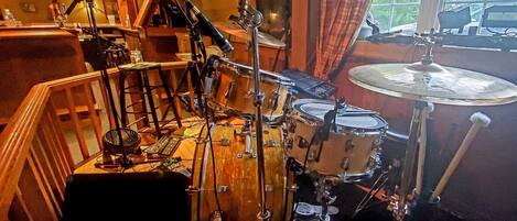 A drum set in a room with a window and a view of a car outside.