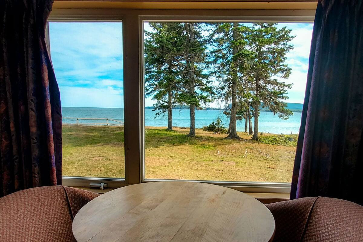A room with a large window offering a view of a grassy area, trees, and a body of water.