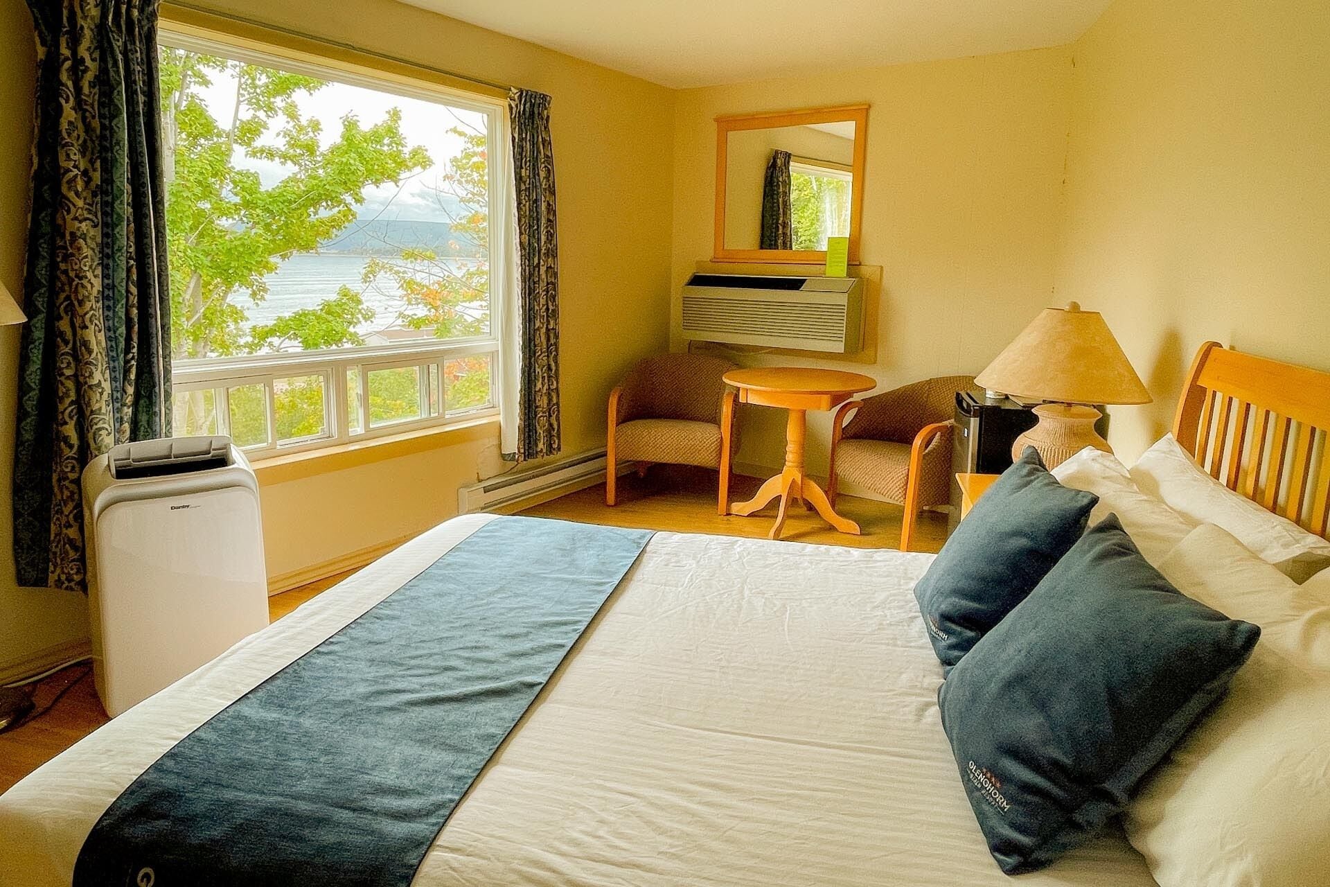 Habitación de hotel con cama, una silla, una mesita, una lámpara y vistas al exterior.