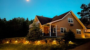A two-story house with a sloped roof, a porch, and a well-lit front yard. - Glenghorm Beach Resort (Ingonish)