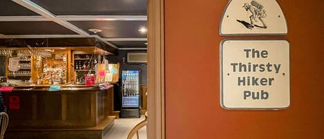 A pub interior with a counter displaying various items, a vending machine, and a sign reading "The Thirsty Hiker Pub".