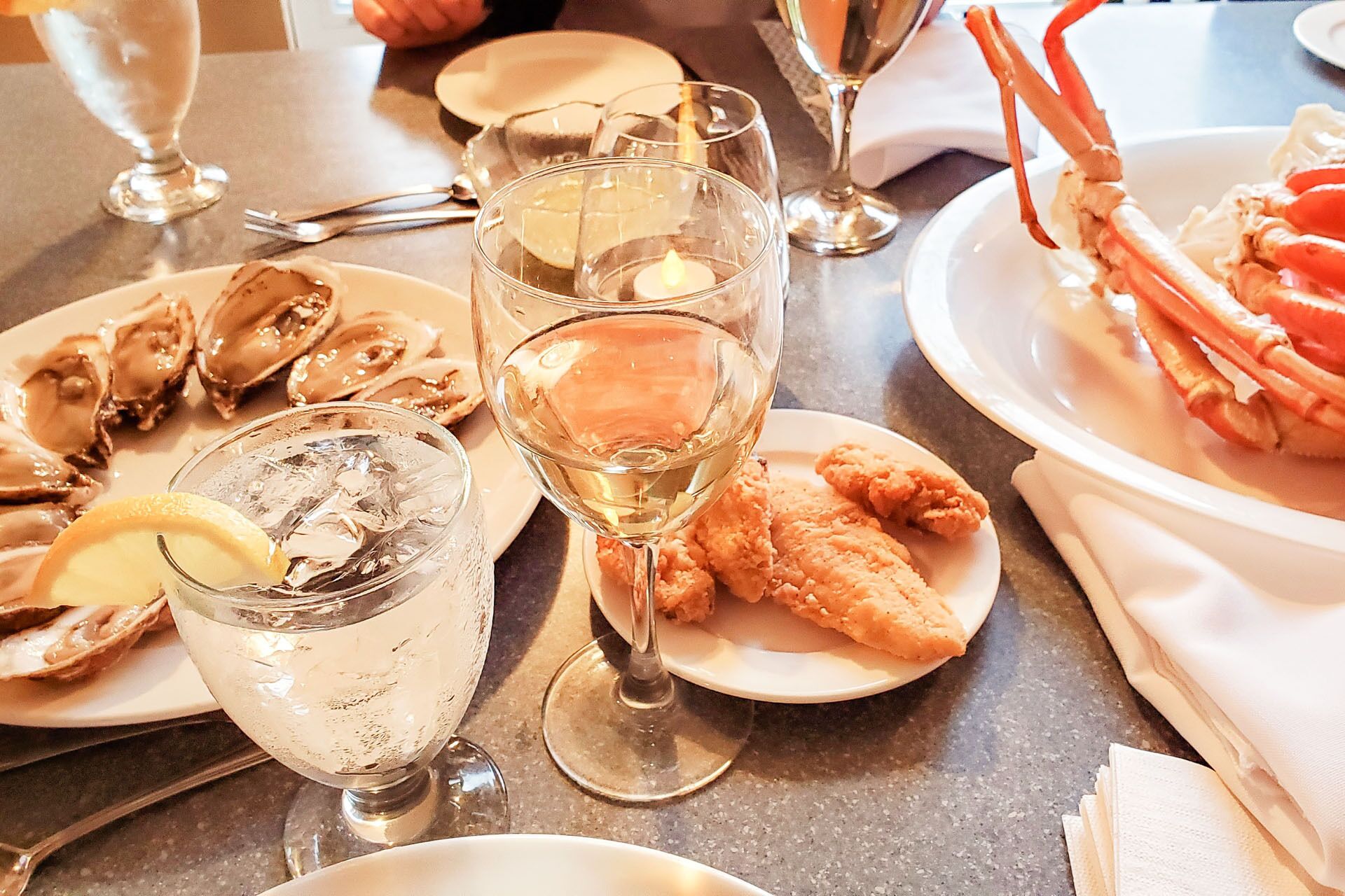 Una mesa de comedor con platos de mariscos, copas de vino blanco y una vela.