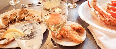 Una mesa de comedor con platos de mariscos, copas de vino blanco y una vela.