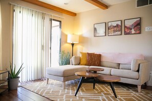 Ein Wohnzimmer mit einer Couch, einem Couchtisch, einer Lampe, einer Pflanze und einem Fenster mit Vorhängen.