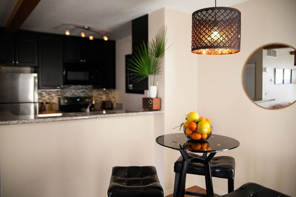 A modern kitchen with dark cabinets, a round dining table with a fruit bowl, and a hanging light fixture.