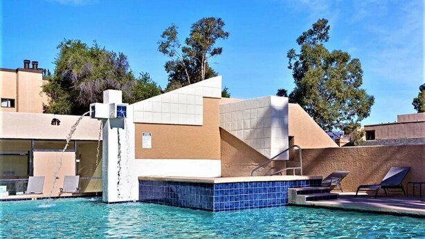 Ett poolområde med modern design, inklusive ett vattenelement och solstolar.