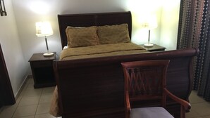 A bed with a wooden headboard, two bedside lamps, a nightstand, and a chair with a cushion.