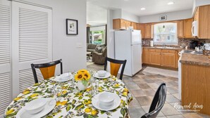 A dining area with a table set for four, a refrigerator, wooden cabinets, and a window in the kitchen.