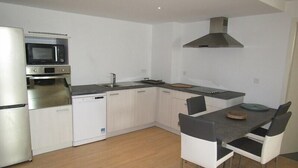 A modern kitchen with white cabinets, a built-in oven, a microwave, and a stove. There is a dining area with a table and chairs. - Nice and spacious ground floor appartment close to the beach (LACANAU OCEAN)