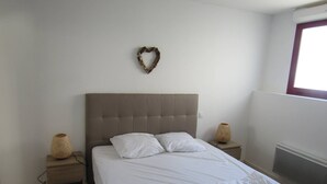 A bedroom with a bed, two bedside tables, a wall-mounted heart decoration, and a window with a view. - Nice and spacious ground floor appartment close to the beach (LACANAU OCEAN)