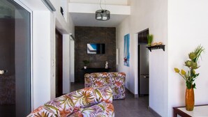 A modern living room with a sofa set, a flat-screen TV mounted on a stone wall, a refrigerator, and a vase with flowers on a side table. - Beachfront House in Playa Tivives with private pool (Tivives)
