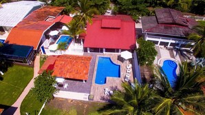 An aerial view of a resort with multiple swimming pools, palm trees, and a variety of roof colors. - Beachfront House in Playa Tivives with private pool (Tivives)