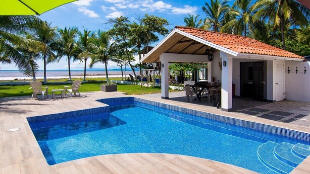 A swimming pool with a tiled edge, surrounded by a covered patio area with outdoor furniture. - Beachfront House in Playa Tivives with private pool (Tivives)