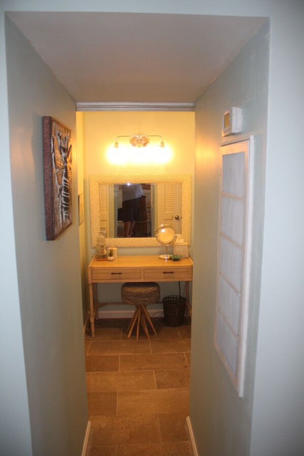 Un couloir étroit avec un coin coiffeuse comprenant un miroir, un luminaire et un petit tabouret.