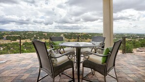 Eine überdachte Terrasse mit Korbmöbeln und einem Tisch, mit Blick auf eine reizvolle Landschaft.
