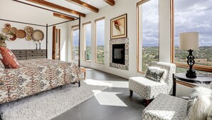 Ein geräumiges Zimmer mit einem großen Bett, einem Kamin und Blick auf die Landschaft durch große Fenster.