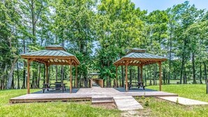 Zwei hölzerne Pavillons mit Picknicktischen in einem bewaldeten Gebiet.