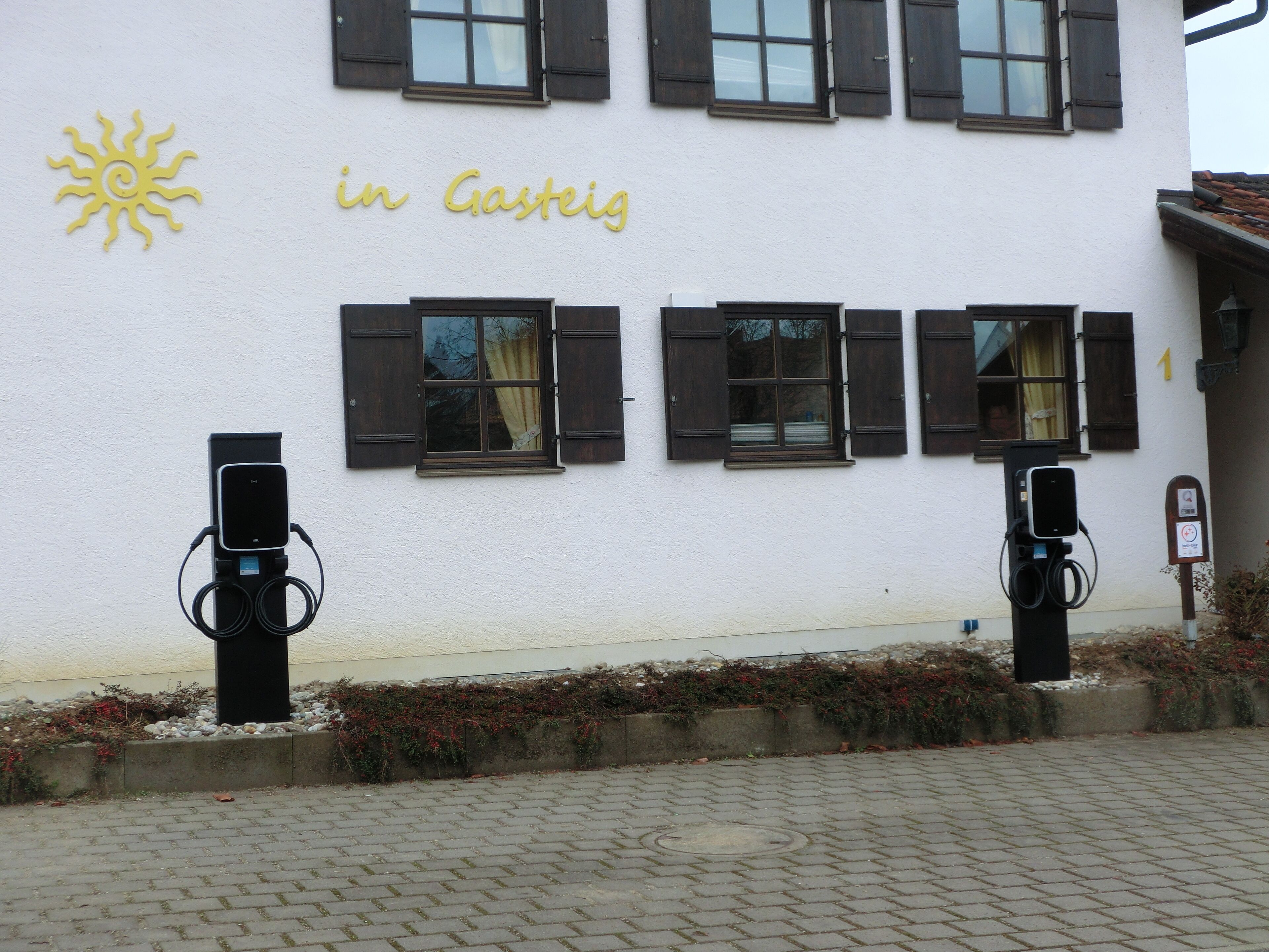 A building with a sign reading 'in Gasteig' and two electric vehicle charging stations.