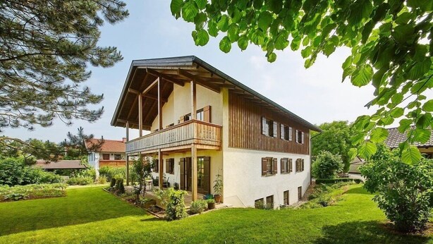 Een huis met twee verdiepingen met een balkon, omgeven door een verzorgd gazon en bomen.