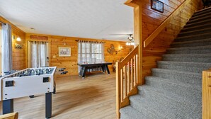 A cozy room with a wooden interior, a foosball table, a ping pong table, and a staircase.