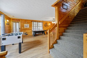 Ein gemütlicher Raum mit Holzvertäfelung, einer Tischfußballplatte, einem Pongtisch und einer Treppe.