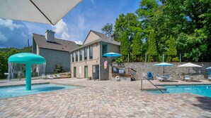A pool area with a brick patio, lounge chairs, and umbrellas.