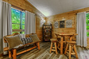 A cozy cabin interior with a wooden bench, a small table, and a bookshelf.