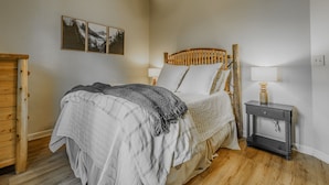 Un dormitorio con cama, mesita de noche, lámpara, cabecera de madera y tres cuadros enmarcados en la pared.