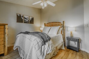A bedroom with a bed, a nightstand, a lamp, a wooden headboard, and three framed pictures on the wall.