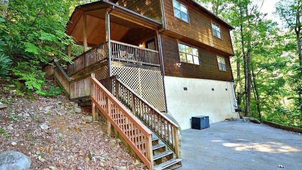 A two-story cabin with a wooden exterior, a balcony on the upper floor, and a staircase leading to the entrance.
