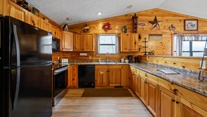 A kitchen with wooden cabinets, a black refrigerator, a dishwasher, and a granite countertop.