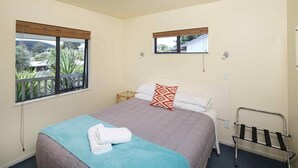 A bedroom with a bed, two windows, a bedside table, and a metal rack.