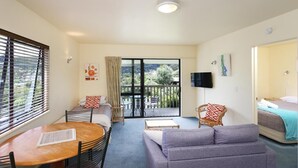 A room with a sofa, a table, a bed, a TV, and a balcony with a view.