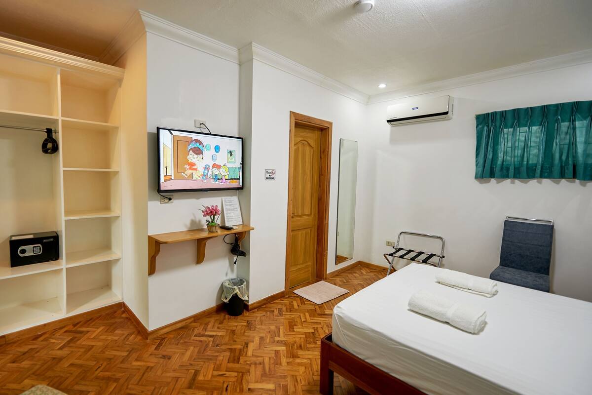 Een hotelkamer met een bed, een televisie, een houten plank, een spiegel en een kledingkast.