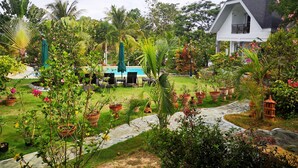 A lush garden with a swimming pool, outdoor seating, and a white house with a dark roof. - Garden Bungalows Resort (Siquijor)