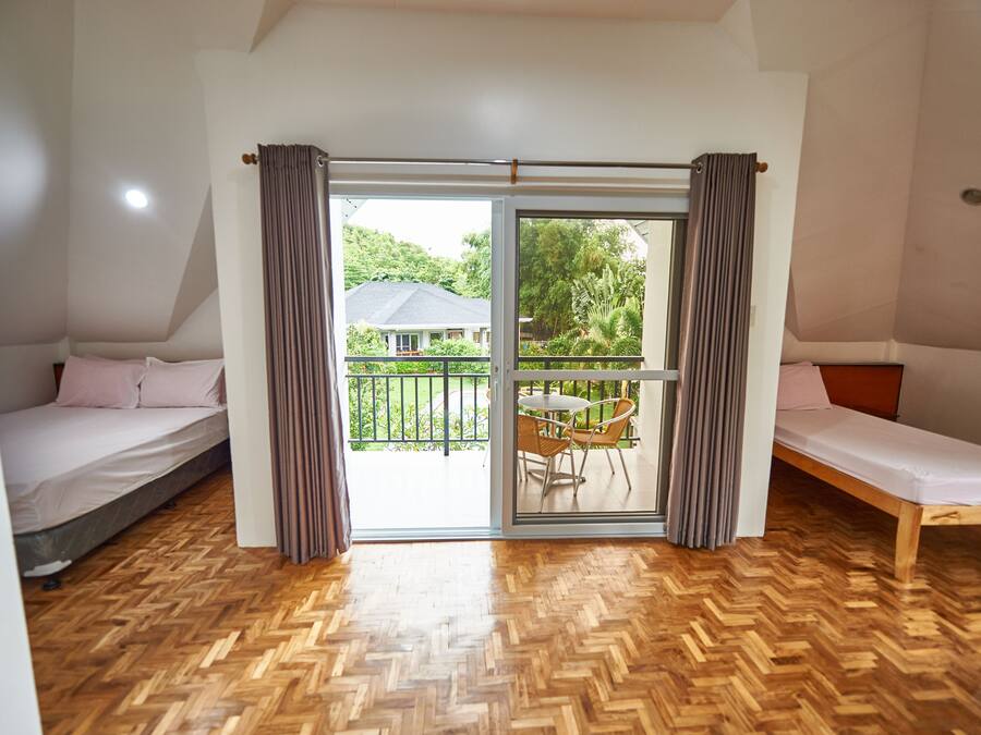 A room with two single beds, a wooden herringbone floor, and a sliding glass door leading to a balcony with a table and chairs.
