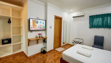 A hotel room with a bed, a TV, a wooden shelf, a mirror, a towel rack, and a wardrobe.