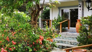 A house with a stone staircase leading to a wooden door, surrounded by lush greenery and flowering plants. - Garden Bungalows Resort (Siquijor)