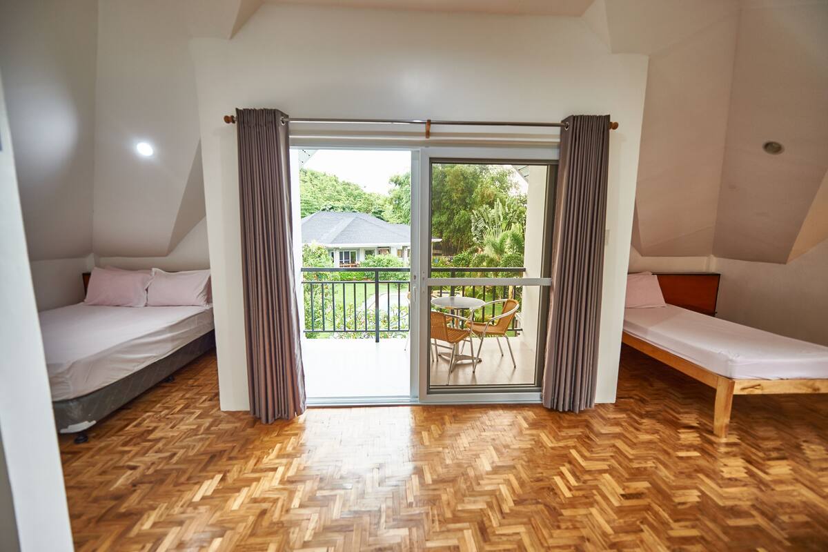 Een kamer met twee bedden, een houten visgraatvloer en een schuifdeur van glas naar een balkon met tuinmeubilair.