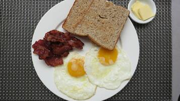 Un plato con tostadas, tocino y huevos fritos sobre un posavasos tejido.